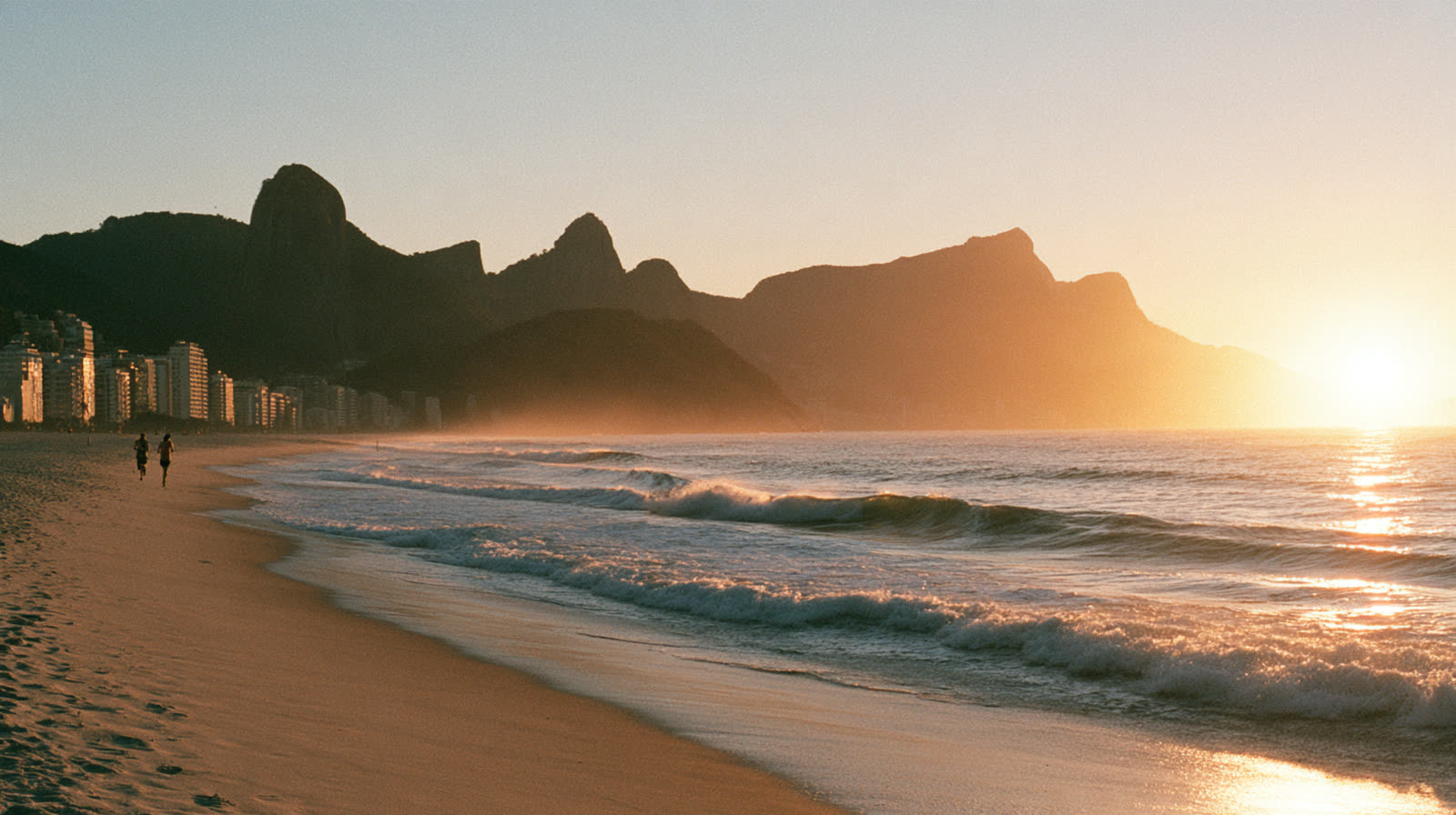 Praia de Ipanema ao amanhecer, com o Morro Dois Irmãos ao fundo e ondas douradas