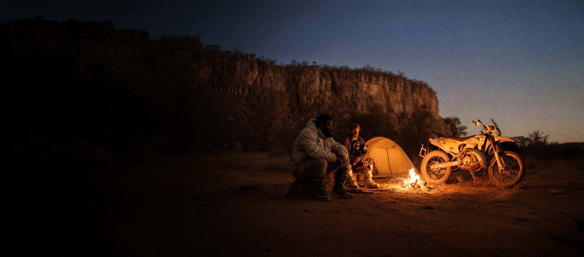 Acampamento ao entardecer com fogueira, barraca e uma moto